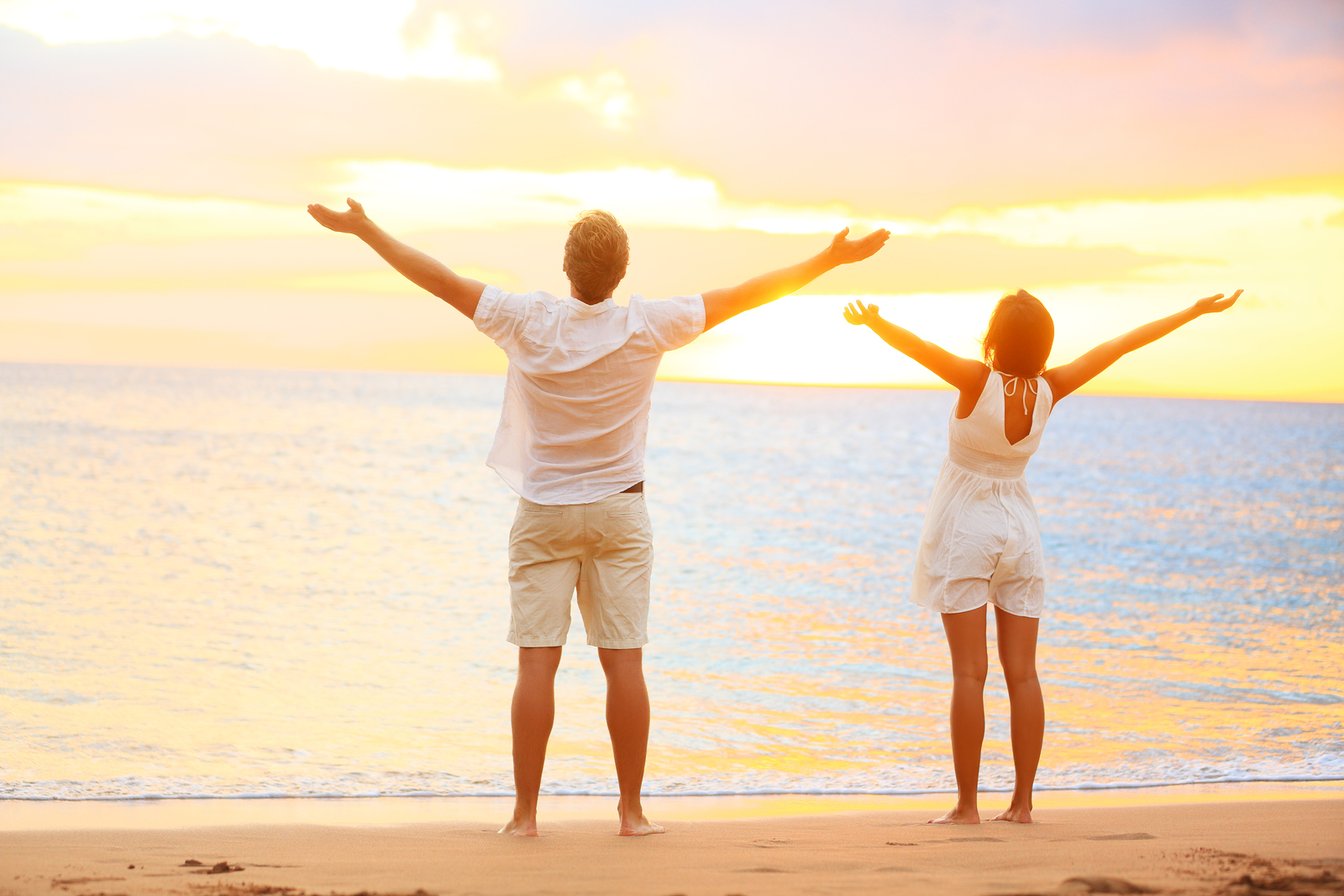 Happy cheering couple enjoying sunset at beach with arms raised - Men